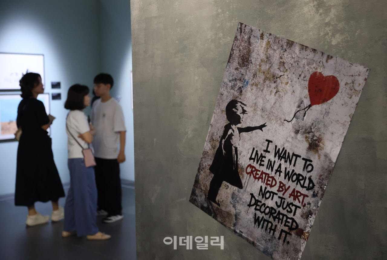 개막일 전시장 안. 거친 콘크리트 벽에 '소녀와 풍선' 패널이 걸렸고, 그 옆을 관람객이 지나간다. 2026년 7월 22일 더현대 서울 ALT.1. ⓒ이데일리