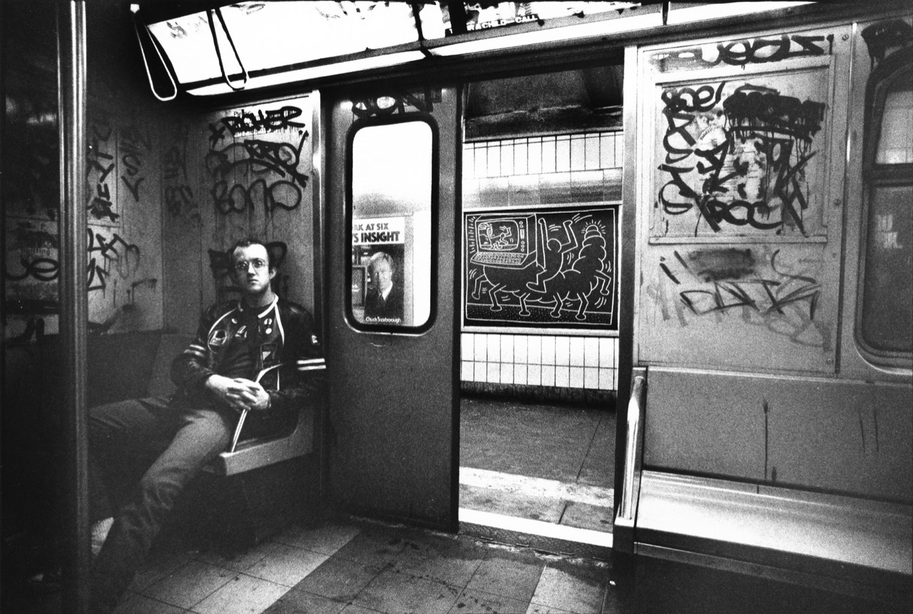 1983년 무렵, 낙서로 뒤덮인 뉴욕 지하철 객차에 혼자 앉은 키스 해링(Keith Haring). 열린 문 너머 승강장 벽에 그가 분필로 그린 드로잉이 붙어 있다. ⓒTseng Kwong Chi / DailyArt Magazine