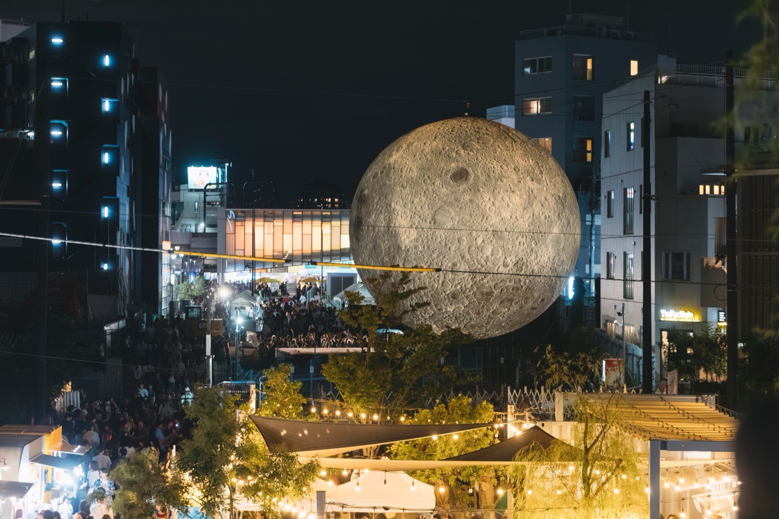空き地に浮かぶ月 · 下北線路街の空き地に掲げられたルーク・ジェラムの「Museum of the Moon」。下ではテントのマーケットが開かれる。ⓒスタートバーン · PR TIMES