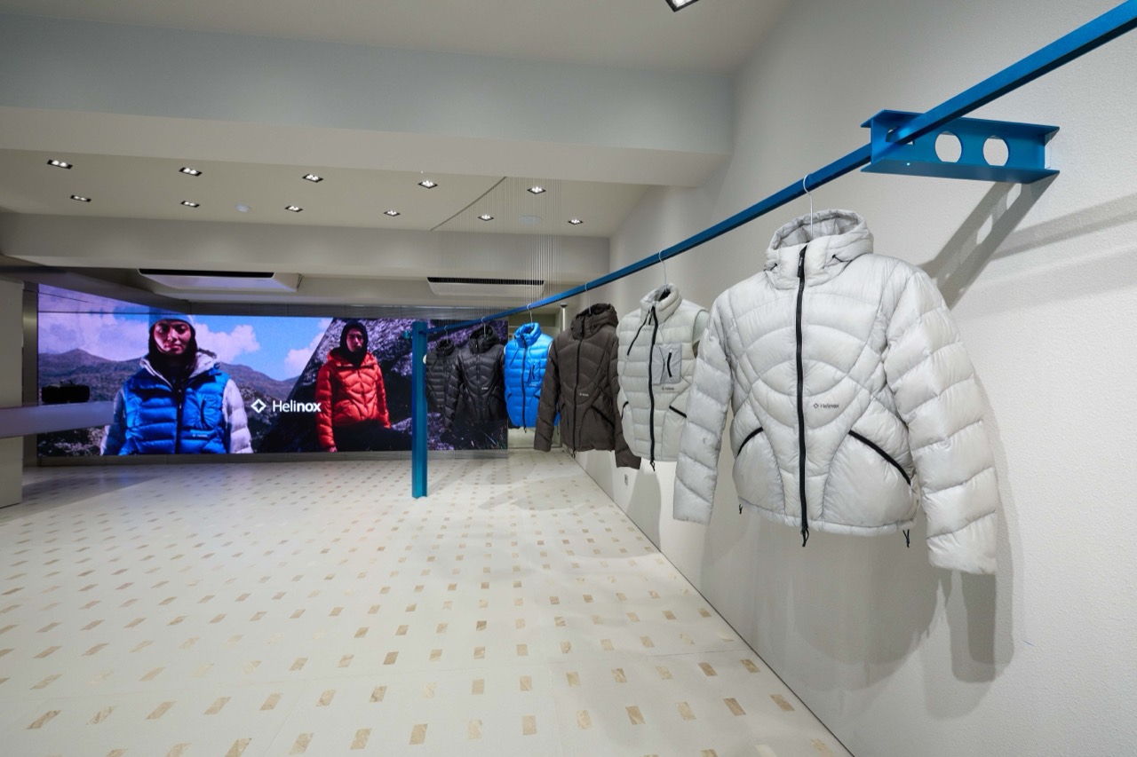 The first-floor media wall · Down jackets hang from a single blue rail, and the wall facing them is a screen from end to end. ⓒKolon FnC