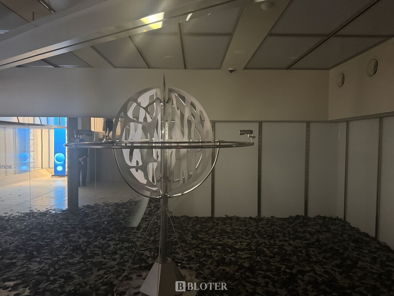 Leaves on the floor · Dry leaves are spread under a sphere made of overlapping metal rings. The structure takes the space that merchandise would. ⓒBloter