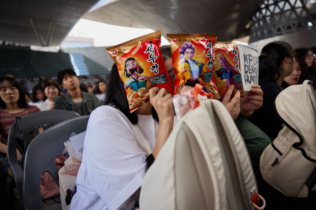 A crowd holding snack bags · Maggie Kang's event in 2025. Audience members held up tie-in snack bags printed with the film's characters. ⓒOuthere505 · CC BY-SA 4.0