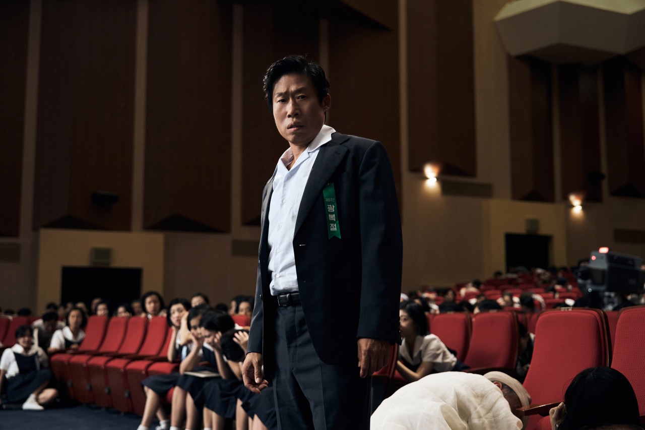 赤い客席 · 赤い座席の間で学生たちが身をかがめ、チョルグが立ったまま周囲をうかがう。ⓒHive Media Corp · News1