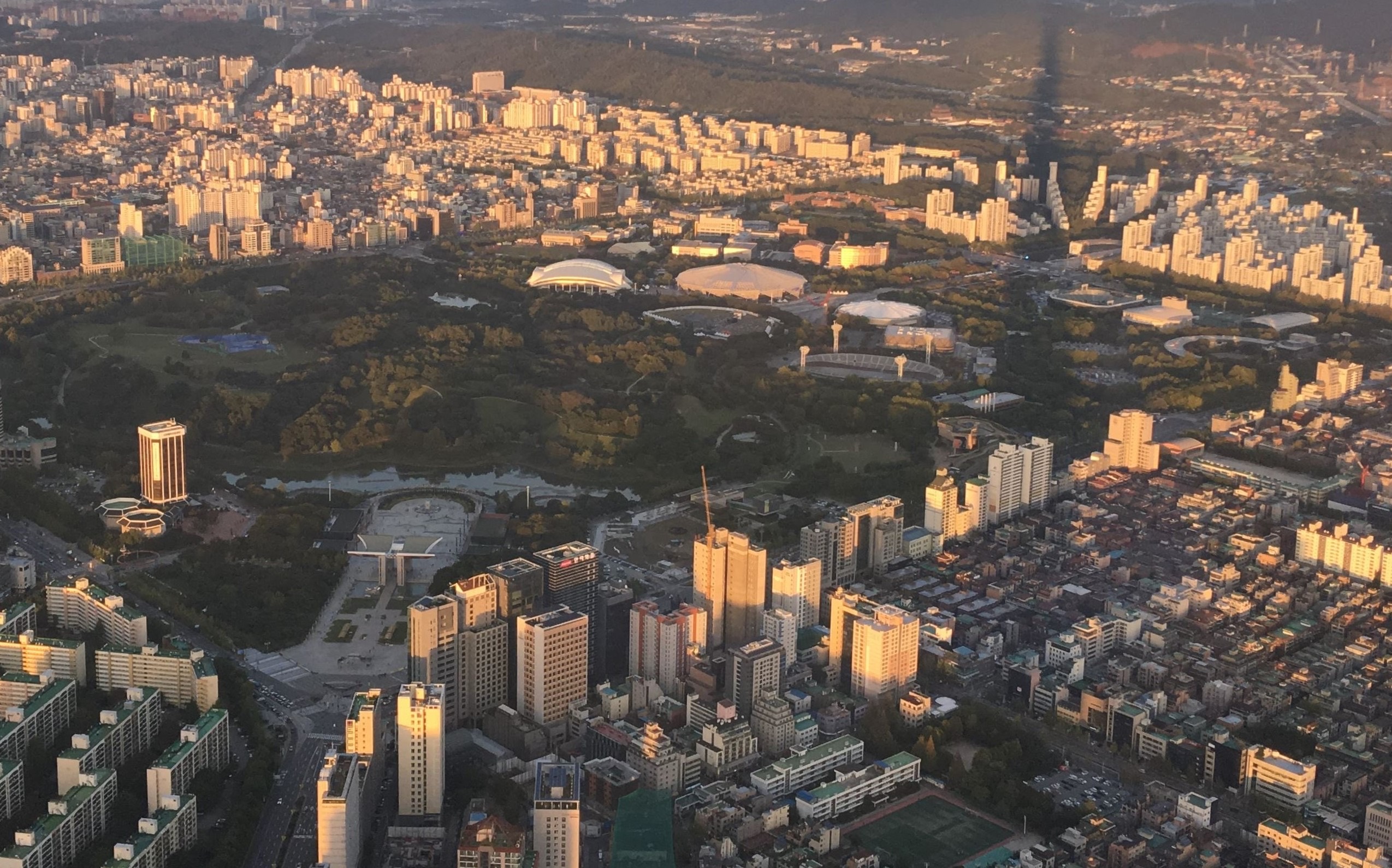 올림픽공원 · 롯데월드타워에서 내려다본 올림픽공원. 숲 사이에 흰 지붕의 경기장들이 흩어져 있다. ⓒChristophe95 · CC BY-SA 4.0