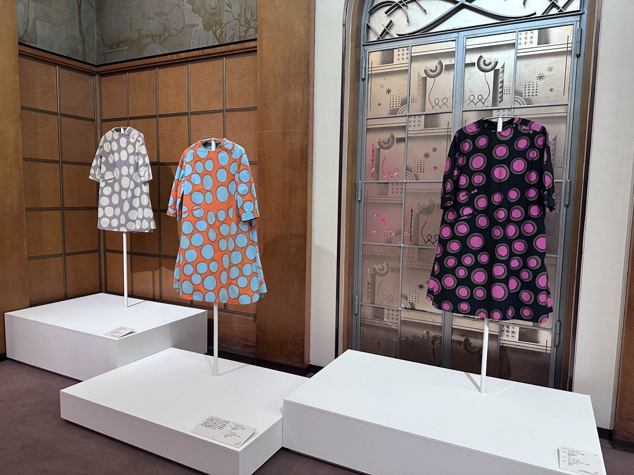ガラス扉の前 · 邸宅の装飾ガラス扉の横に、円の柄と花柄のワンピースを立てた。ⓒFASHIONSNAP