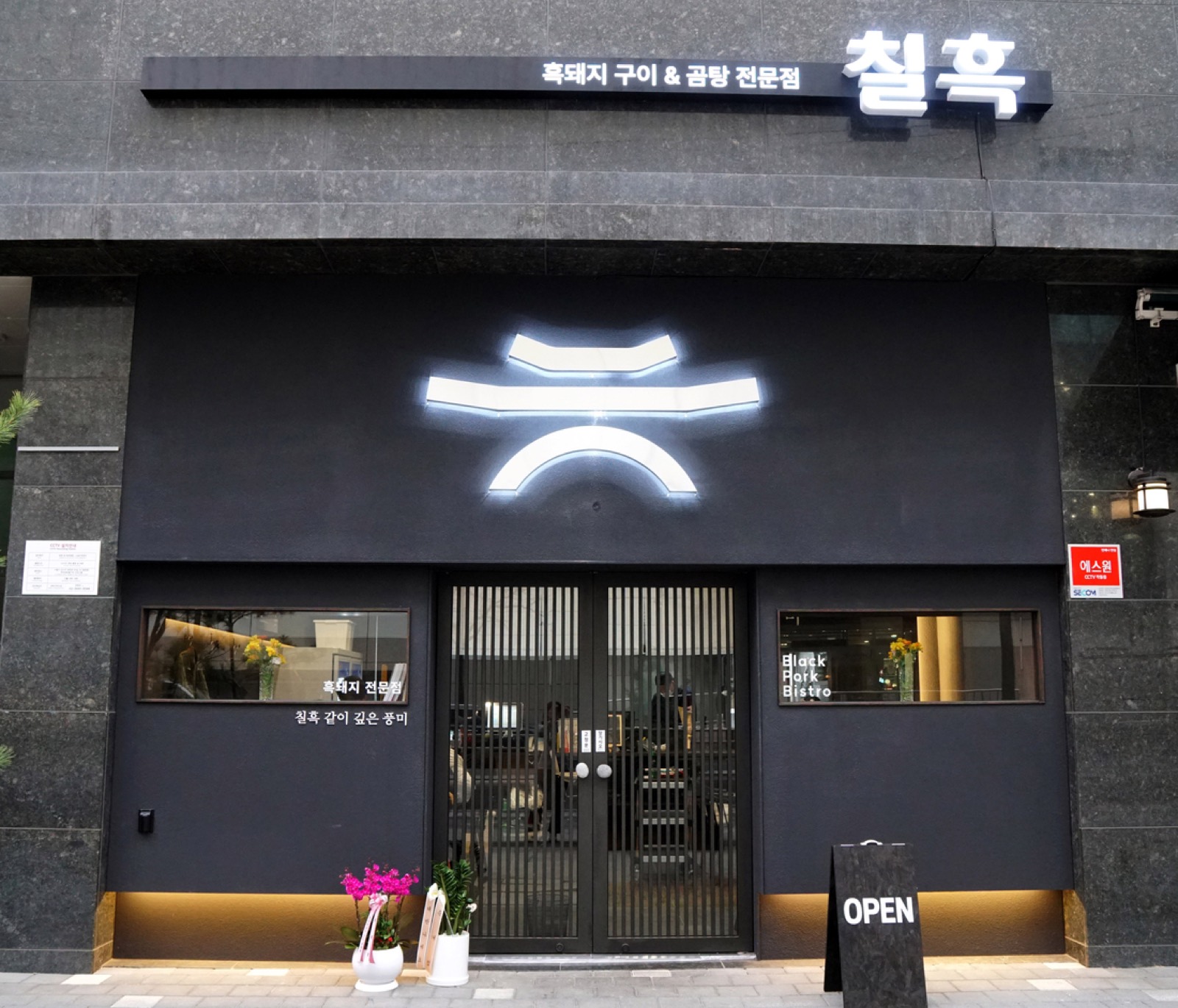 등촌동 화곡로66길 · 간판에 「흑돼지 구이 & 곰탕 전문점」, 오른쪽 유리창에 Black Pork Bistro. 문 앞에 OPEN 입간판이 서 있다. ⓒ경향신문