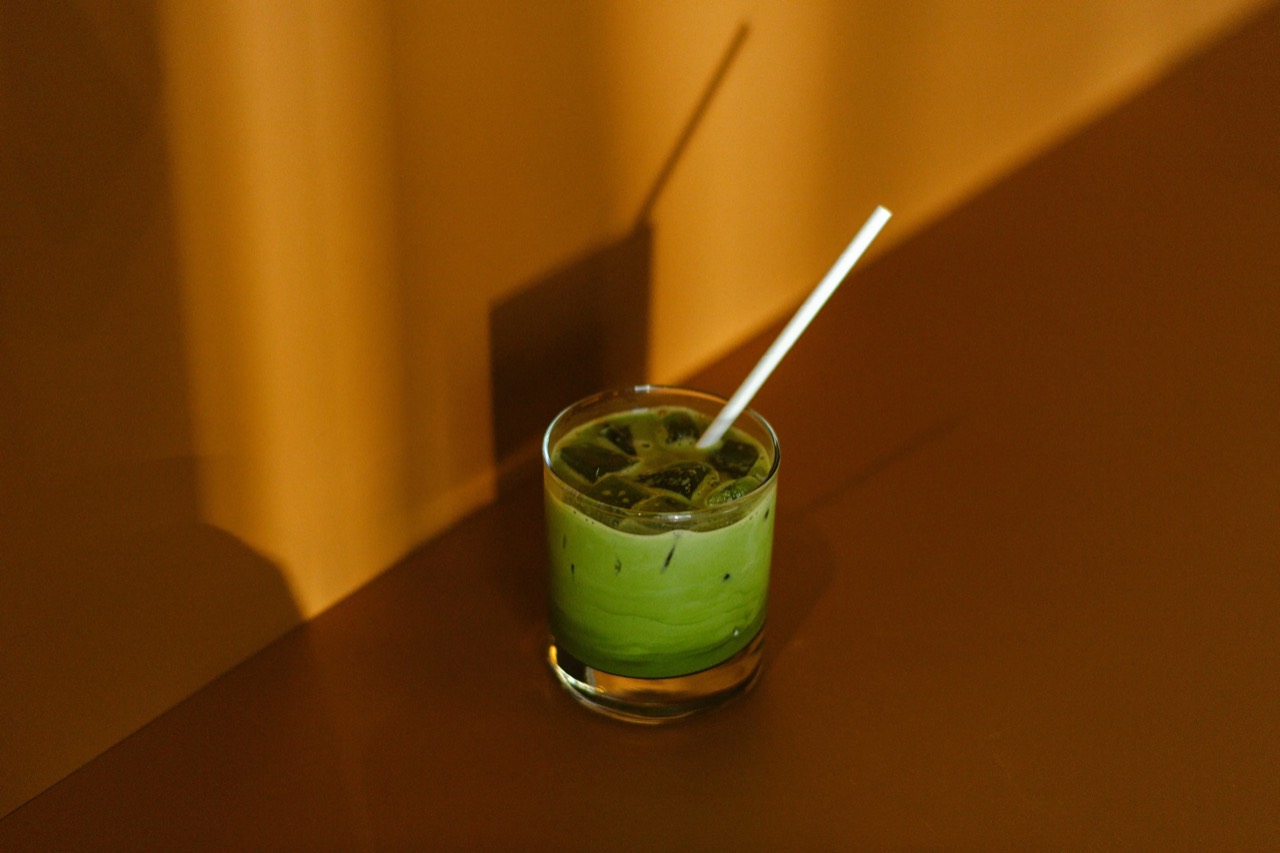 Yuzu honey matcha · The matcha poured over ice has not yet mixed with the milk below. Afternoon light falls in hard angles across the back of the banquette. ©Yusuke Oba · Broadsheet