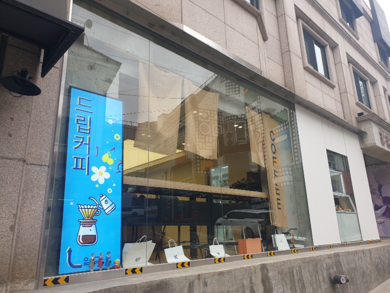 通りから見えるもの · 青い縦看板と、ガラス越しのグッズ陳列。道が坂なので店の床が歩道より高い。ⓒAwesomeWaves