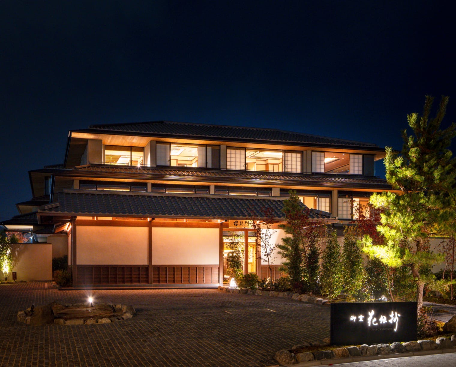 The exterior at night · After dark, warm lights come on under the eaves and in the windows. With no parking, the forecourt holds only gravel and the sign. ⓒKyoritsu Maintenance