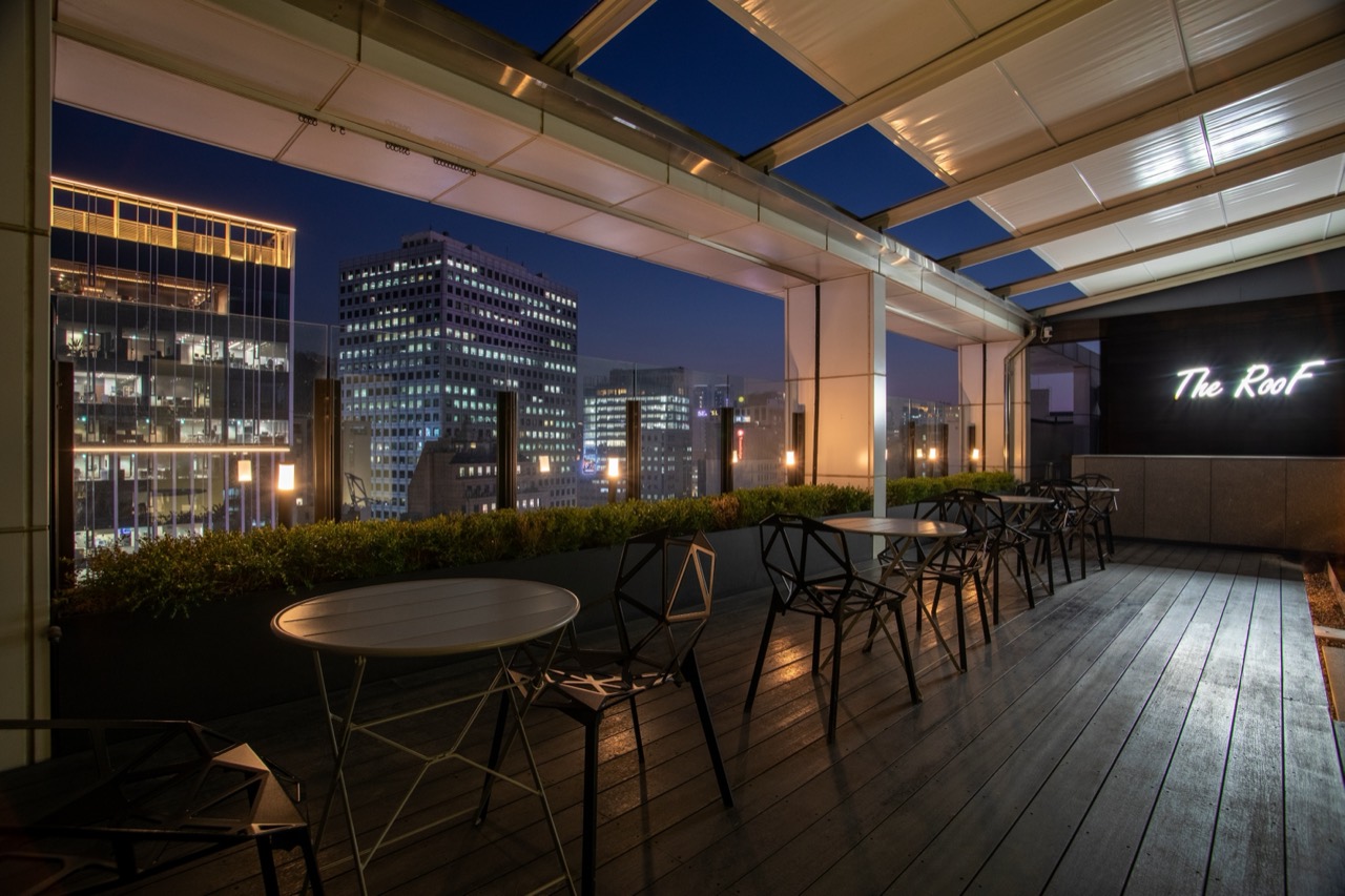 옥상 테라스 The Roof · 나무 데크에 금속 탁자와 철제 의자를 놓았고, 난간 너머로 을지로 일대 사무 빌딩이 보인다. ⓒHOP INN · Eats Me, Jax!
