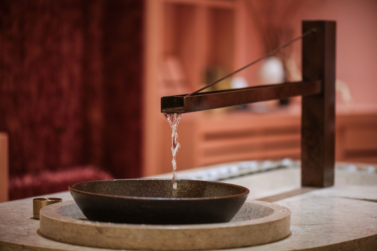 水を落とす管 · 青銅色の管から落ちた水を石の鉢が受ける。背後は赤いベルベットの壁。ⓒPAÑPURI
