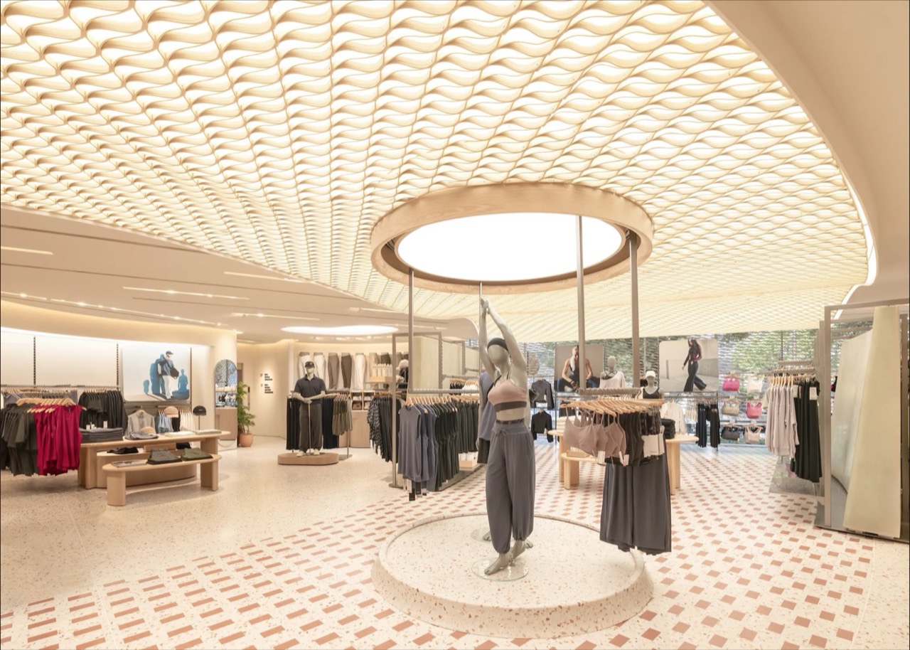 The ceiling gets your attention first · Light runs between the waves of the timber ceiling, and on the central round platform a mannequin reaches up to the lighting ring. ⓒlululemon
