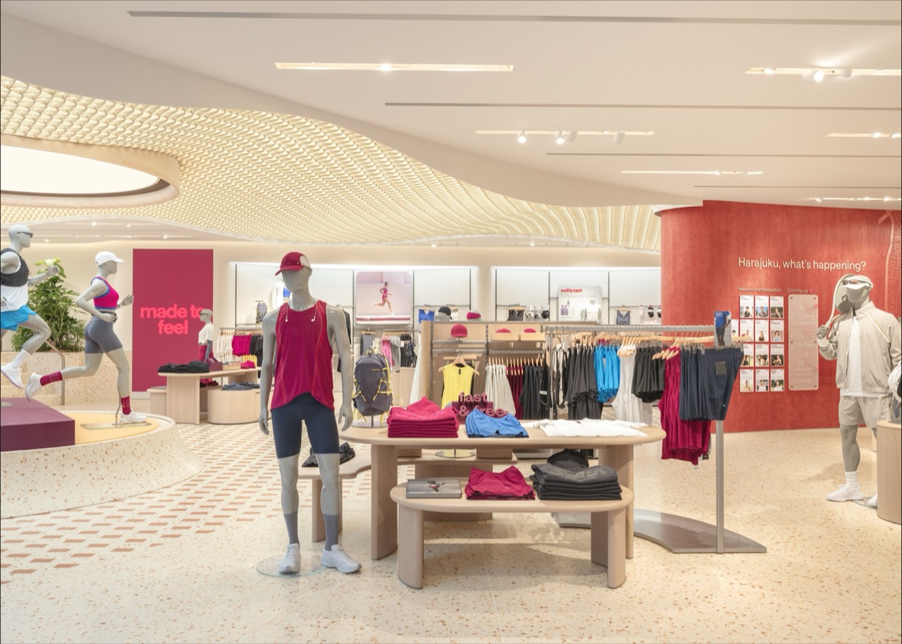 Posed mid-stride · The ground floor. Past the timber tables, the red plane on the right is the ambassador wall; the pink panel on the left reads 'made to feel'. ⓒlululemon