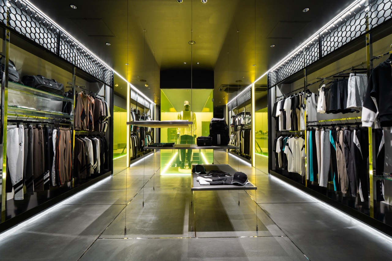 Ground-floor aisle · Racks fill both walls and the center is left open. Yellow light comes from inside the display bays. ⓒ大阪ミナミジャーナル