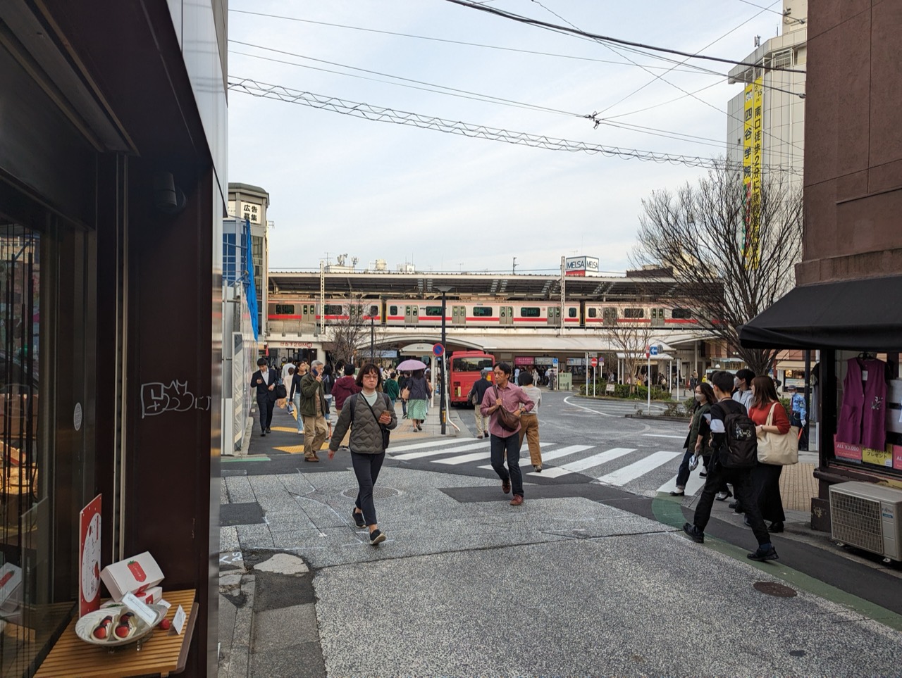 駅前 · 高架の下にバスが停まり、その脇の歩道は人が二人並べる幅だ。ⓒSyced · CC0