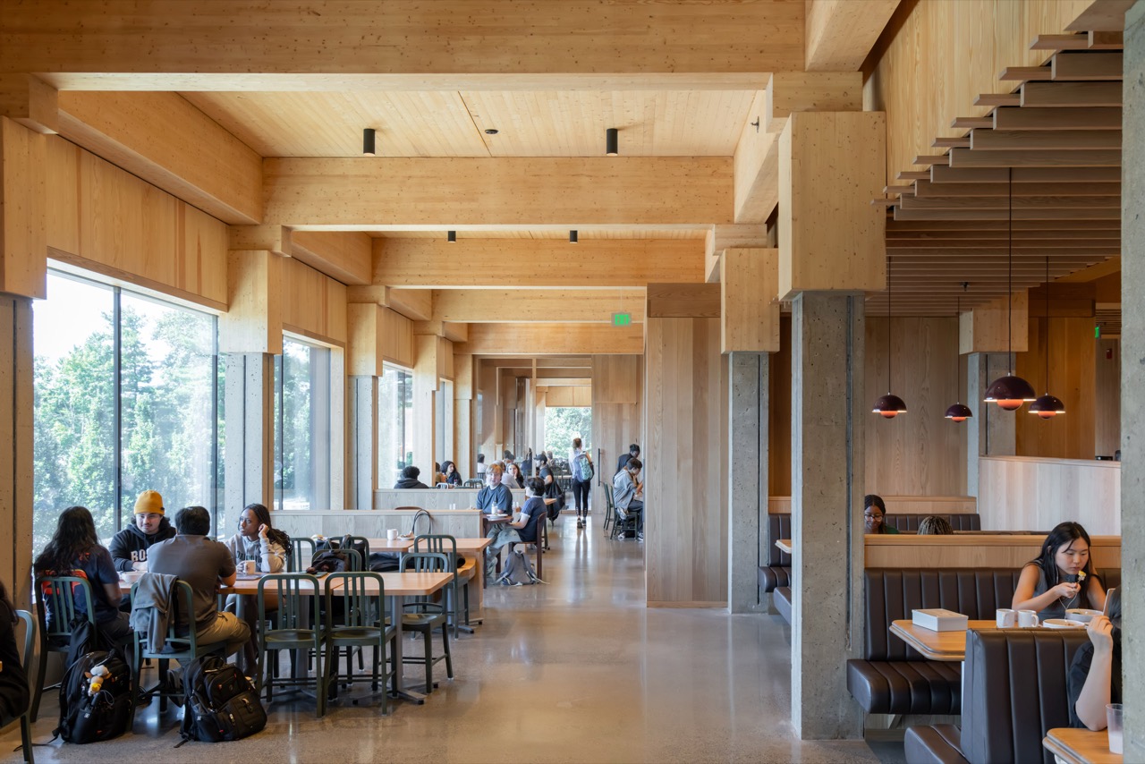 食堂ホール · 古いコンクリートの柱の上を新しい木の梁が渡る。窓際は長テーブル、奥はブース席。ⓒIwan Baan · Dezeen