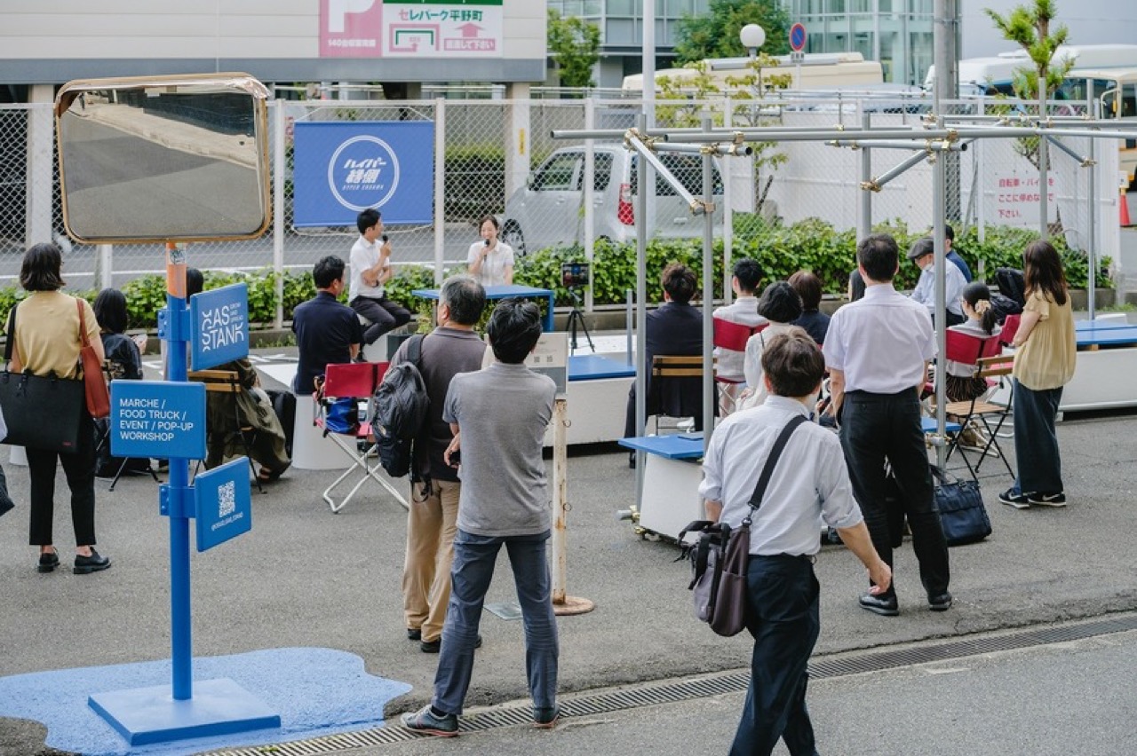 仕事帰りのトークイベント · シャツ姿の会社員が立ったまま話を聞く。ⓒYosuke Ohtake