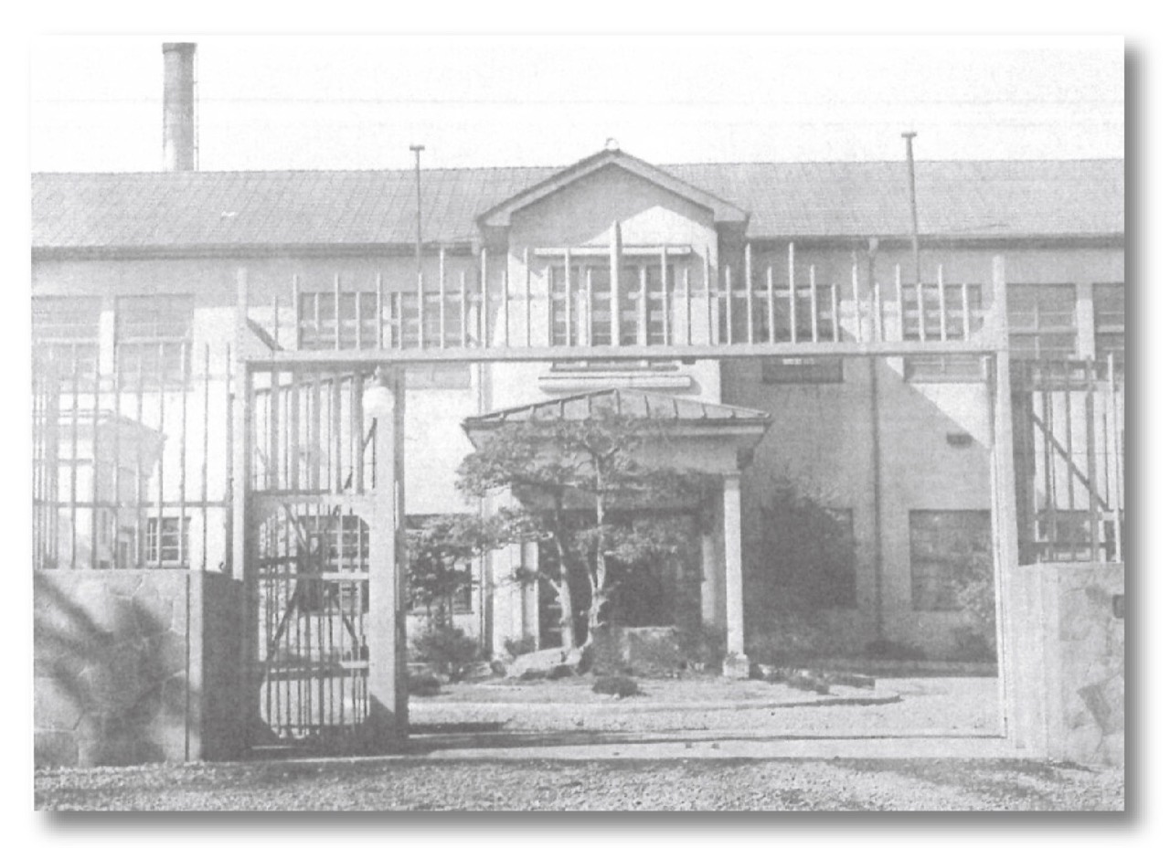 旧刑務所の正門 · 二本の門柱の間に鉄格子の扉が閉じている。ⓒ八王子ミライテラスパートナーズ · 八王子駅南口集いの拠点