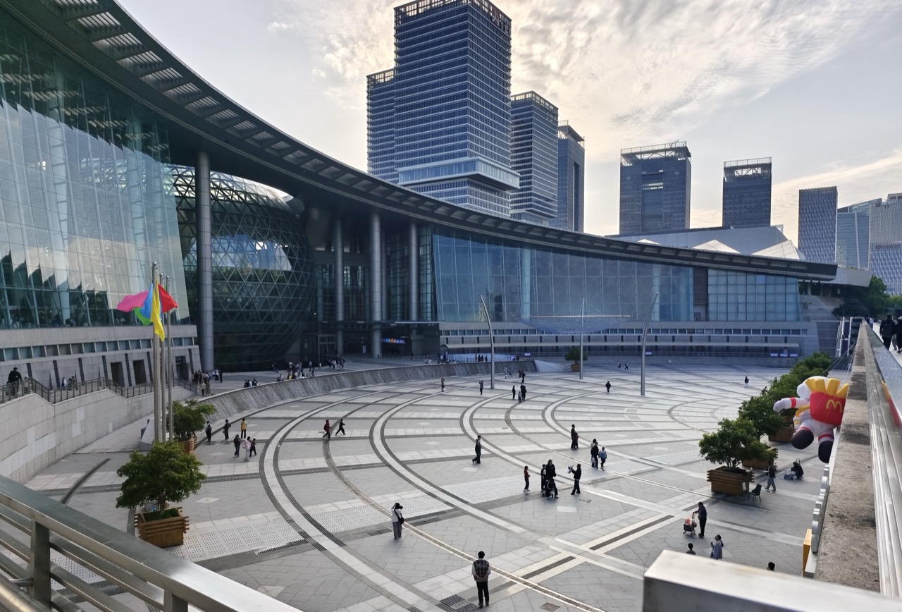 The front, seen from the plaza · The curved roof wraps the plaza, with Pudong's towers rising behind. ⓒDvTor8303 · Wikimedia Commons (CC0)