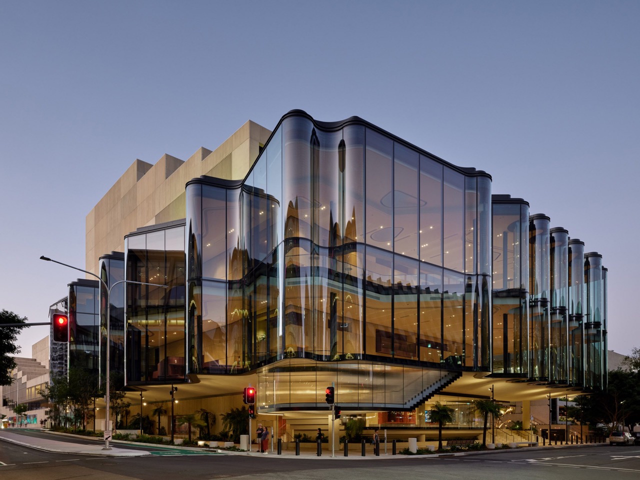 The corner from the intersection · Behind the glass, a sand-coloured mass rises in steps. It holds the auditorium and the stage. ⓒChristopher Frederick Jones · via Dezeen